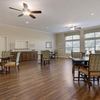 A spacious interior dining area with wood flooring, furnished with tables and chairs, large windows, and a ceiling fan.
