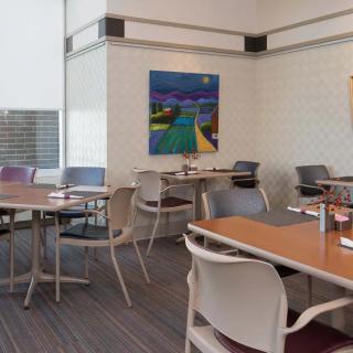 A modern restaurant interior with tables and chairs, featuring colorful artwork on the wall.