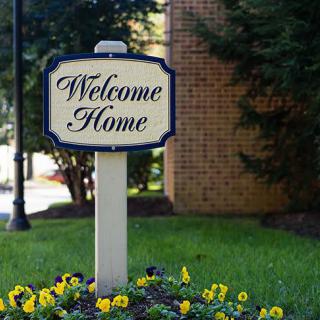 A 'Welcome Home' sign in a garden setting with blooming flowers.