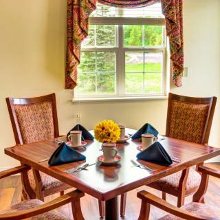 A cozy dining area with a wooden table set for four, featuring flowers and napkins, near a window with a view.