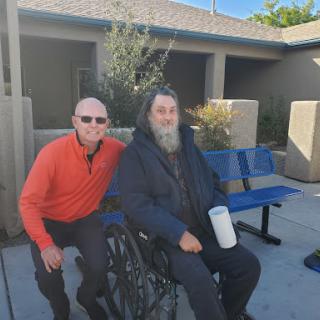 Two men enjoying a sunny day outdoors, one seated in a wheelchair.