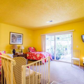 A brightly colored bedroom with yellow walls, featuring a single bed, chair, and sliding glass door.