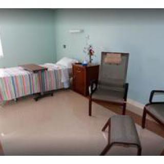 A simple hospital room with a bed, chairs, and a small table.