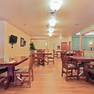 A spacious restaurant dining area with wooden tables and chairs, warmly lit under ceiling lights.