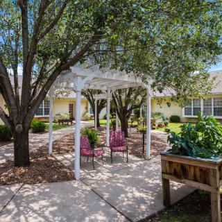 A peaceful garden setting with a pergola, surrounded by trees and seating.
