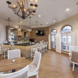 A modern restaurant interior featuring a dining area with tables and chairs, a bar, and decorative chandeliers.