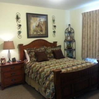 A cozy bedroom with a neatly made bed, decorated with a painting and lamps.