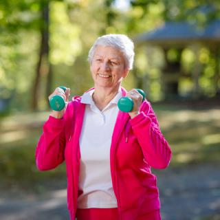 An elderly woman exercising with small dumbbells outdoors.