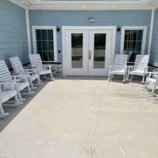 White rocking chairs arranged outside a building with double doors.