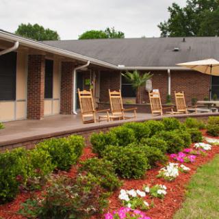 A tranquil outdoor space featuring a cozy patio with rocking chairs and vibrant flower beds.