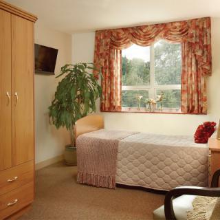 A cozy bedroom with a single bed, wardrobe, and a window adorned with floral curtains.