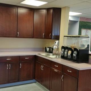 An office kitchen with wooden cabinets and a coffee machine on the countertop.