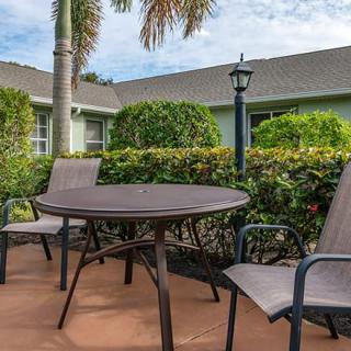 A cozy outdoor patio with a table and chairs, surrounded by lush greenery and a lamp post.