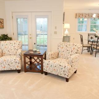 A cozy living room with two patterned armchairs, a wooden coffee table, and large windows in the background.