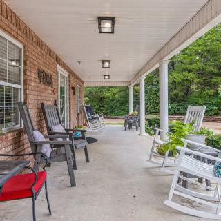 A spacious covered porch with various chairs, including rocking chairs, alongside a brick wall.