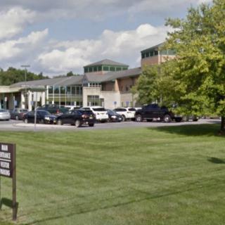 A view of a modern building with cars parked in front and a green lawn.