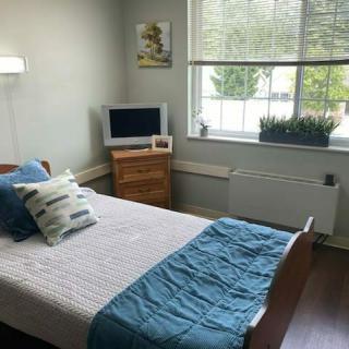A cozy bedroom with a neatly made bed, a small TV on a wooden dresser, and a window with natural light.