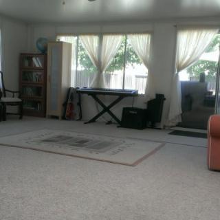 A spacious living room with a piano, bookshelf, and large windows letting in natural light.