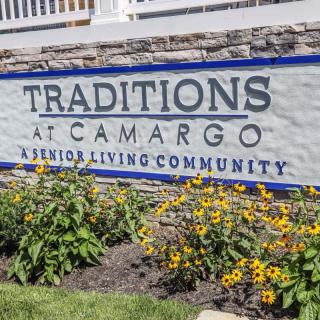 Entrance sign for Traditions at Camargo Senior Living Community surrounded by flowers.