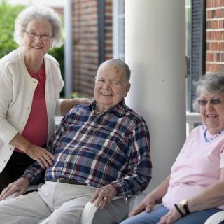 A group of elderly individuals sitting together outside and smiling.