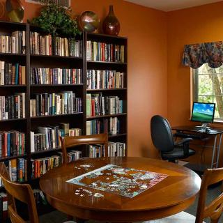 A cozy home library with bookshelves, a table with a puzzle, and a computer by the window.
