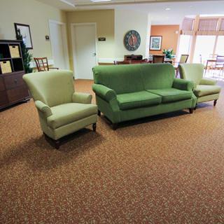 A cozy living room with a green sofa and armchairs on a brown carpet.