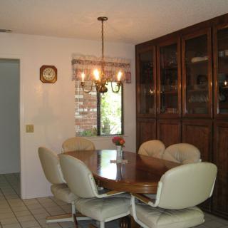 A dining room with a wooden table, upholstered chairs, and a chandelier under natural light from the window.