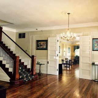 A beautifully designed interior with a wooden staircase, open doors leading to a dining area, and a chandelier hanging from the ceiling.