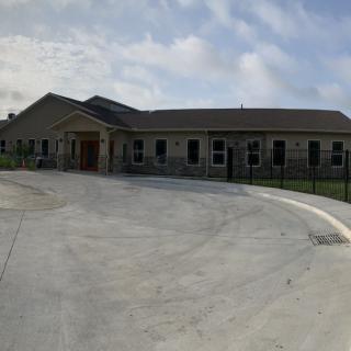 A single-story building with a wide driveway and a cloudy sky overhead.