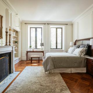 A well-decorated bedroom with a cozy ambiance, featuring a bed, fireplace, and large windows.