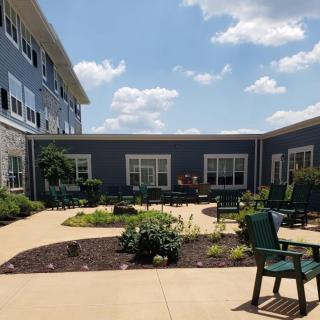 A charming courtyard garden with seating, surrounded by a modern building under a blue sky with clouds.
