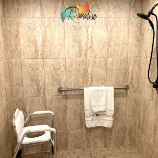 An accessible bathroom with a walk-in shower, featuring a handheld showerhead, seat, and towel rack.