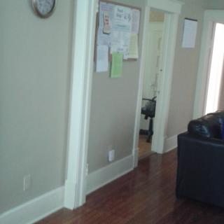 A view of a living room with a hallway, featuring a notice board, sofa, and wall clock.