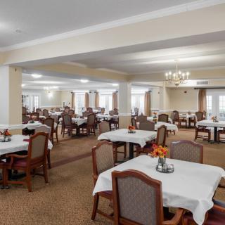 Spacious dining room with multiple tables and chairs, elegantly decorated with white tablecloths and a chandelier.