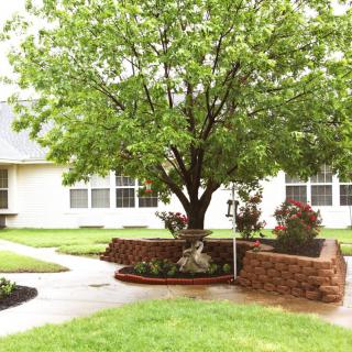 A landscaped garden featuring a large tree surrounded by a circular brick wall, with well-maintained lawns and pathways.