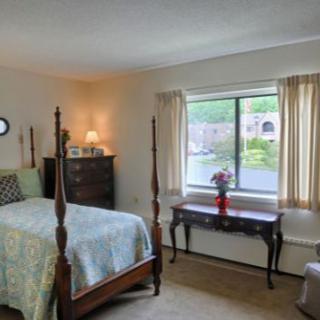 A cozy bedroom features a four-poster bed and traditional furniture, with a window view and decorative flowers on a table.