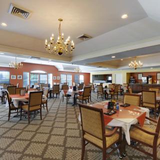 A spacious dining area with multiple tables and chairs, elegantly decorated with chandeliers.