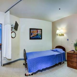 A simple hospital room with a single bed, television, and dresser.
