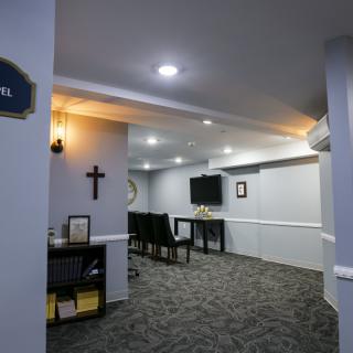 A small chapel interior with seating, a cross on the wall, and modern lighting.