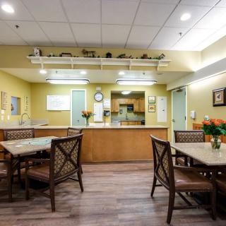A cozy dining area with tables, chairs, and a view of the kitchen, decorated with flowers.