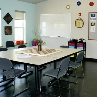 A clean and organized classroom or meeting room with a central table, chairs, a whiteboard, and decorations on the wall.
