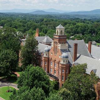 An aerial view of a historic building surrounded by lush greenery and distant mountains.