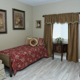 A cozy bedroom with a single bed, decorative pillows, side table, and wall art.