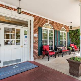 A welcoming porch with red-cushioned chairs and a brick wall backdrop.