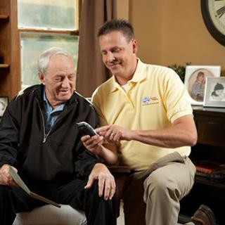 A caregiver assisting an elderly man with a device in a cozy home setting.