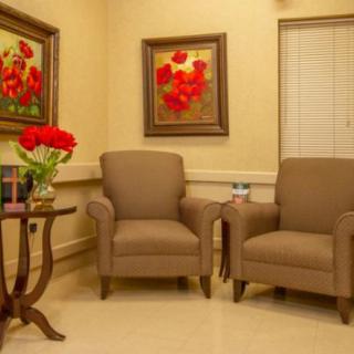 A cozy waiting room with two armchairs, a small table with a lamp and flowers, and framed artwork on the walls.