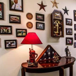 A cozy home interior features a wall adorned with framed photos and military memorabilia, including a flag display case and a vintage clock.
