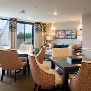 A modern and elegantly decorated living room with a dining area, featuring comfortable chairs and large windows.