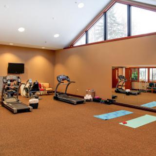 A well-lit fitness room equipped with various exercise machines and yoga mats.