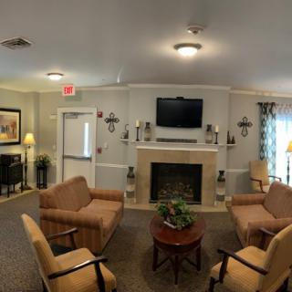 A cozy living room with four armchairs arranged around a central coffee table, featuring a fireplace with a television mounted above it.